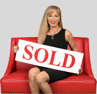 Linda Craft in 2018 - sitting on red couch holding a 'Sold' sign
